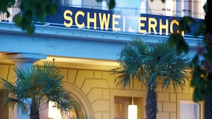Un bâtiment sur lequel on peut lire l’inscription « SCHWEIERHOF », avec des palmiers devant.