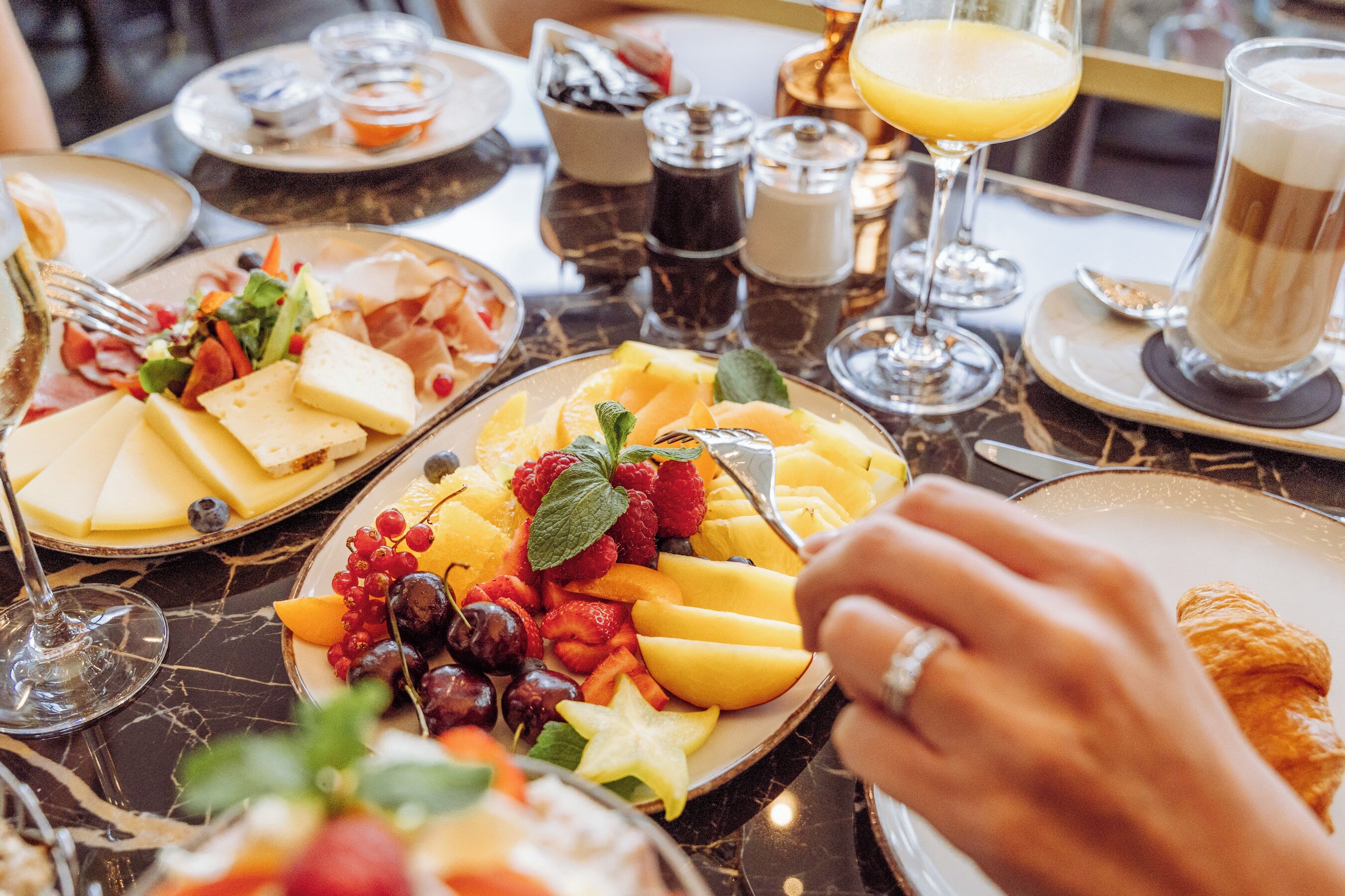 A breakfast setting with plates of cheese, fruits, and pastries on a marble table.