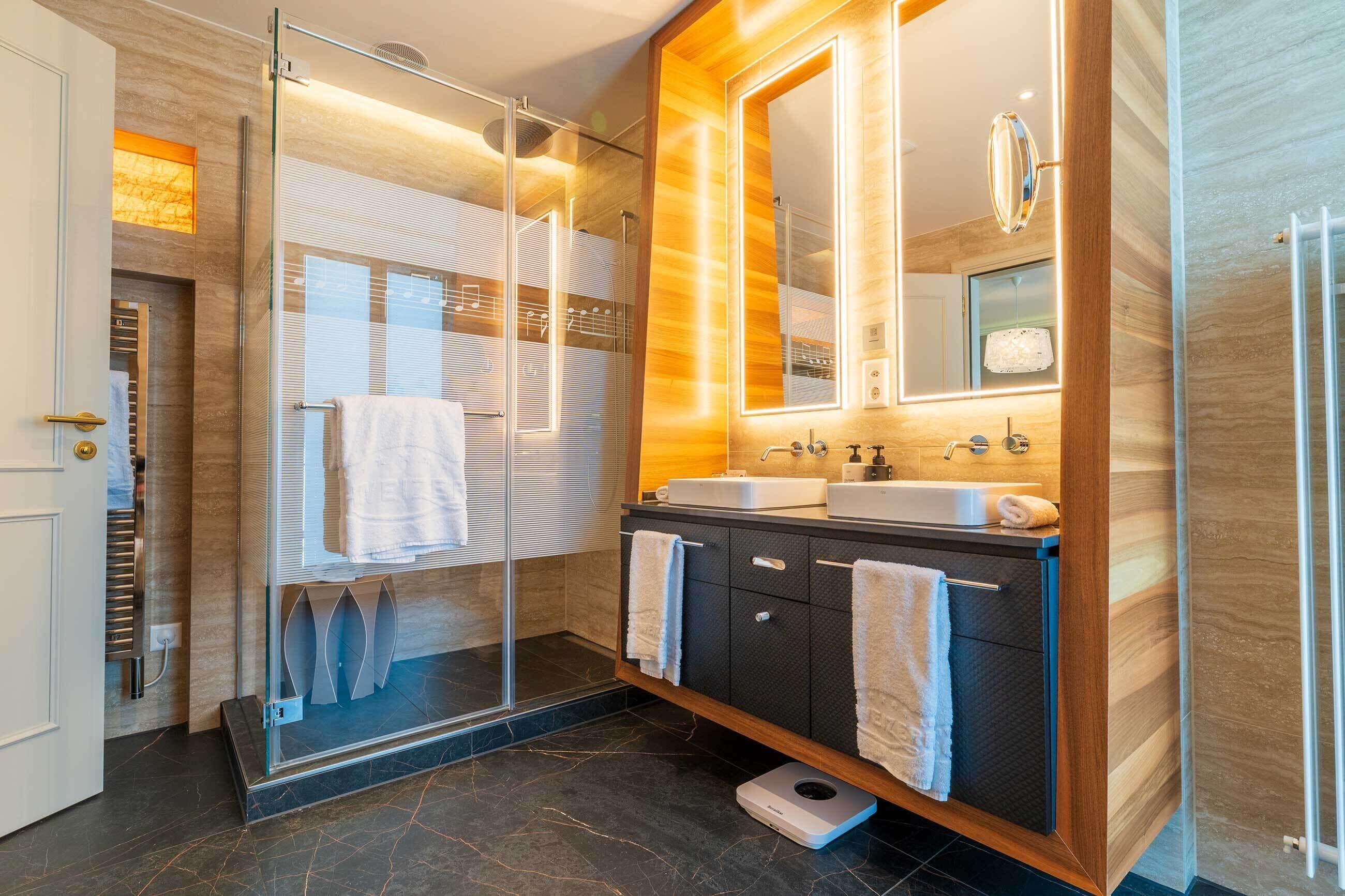A modern bathroom with a glass shower enclosure, dual sinks, and a large mirror.