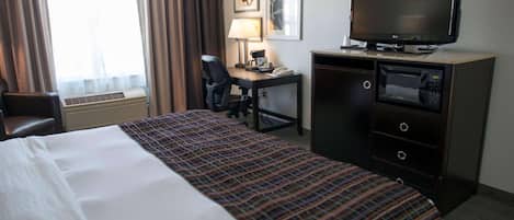 Habitación de hotel con cama, escritorio, computadora, televisor, microondas y una silla.