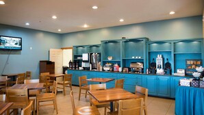 A restaurant with wooden tables and chairs, a coffee bar with various appliances, and a TV mounted on the wall. - Country Inn & Suites by Radisson, Effingham, IL (Effingham)
