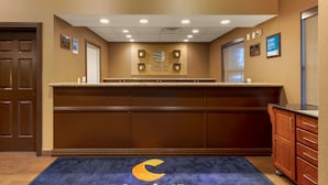 A reception area with a counter, a blue carpet with a crescent moon design, and a wall-mounted sign. - Comfort Inn & Suites Fayetteville - University Area (Fayetteville)