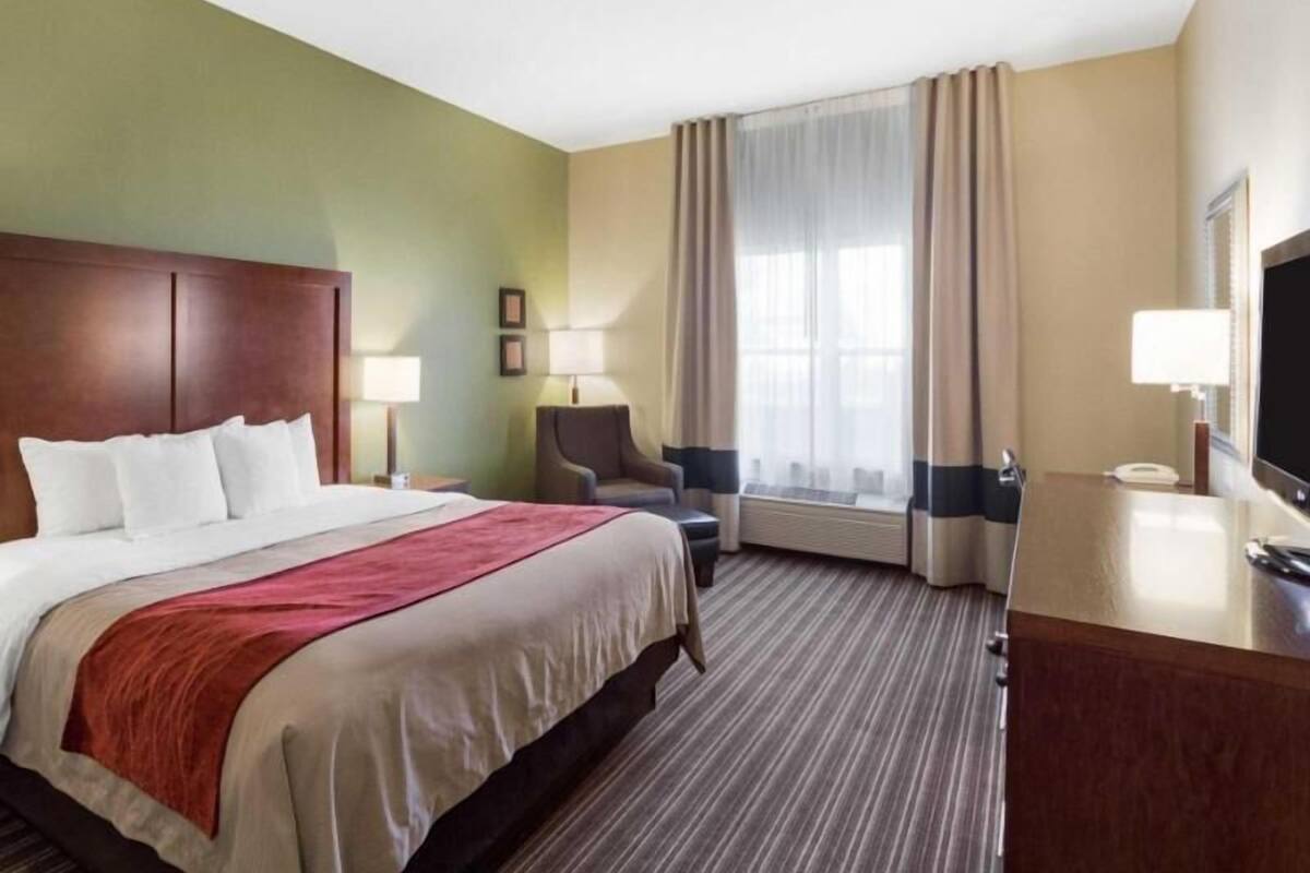 A hotel room with a bed, a desk, a chair, a TV, and a window with curtains.