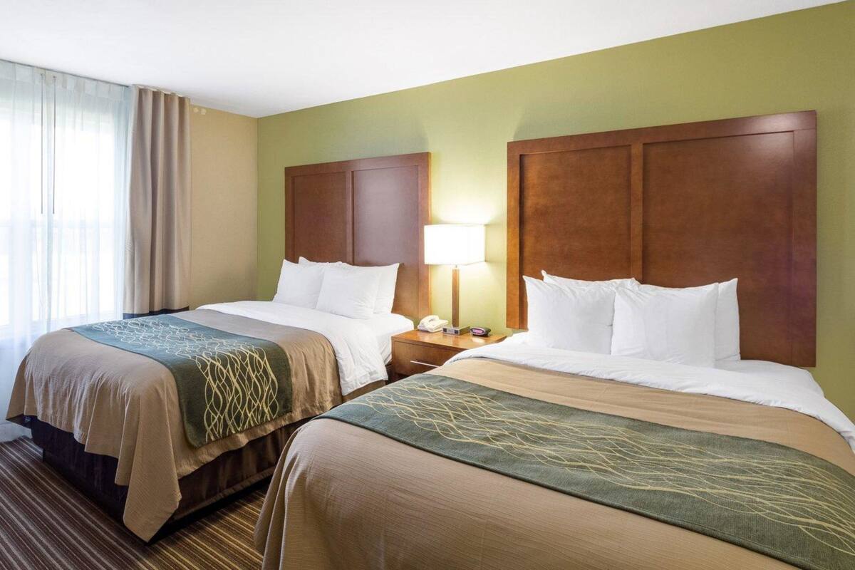 A hotel room with two beds, a nightstand with a lamp, and a window with curtains.