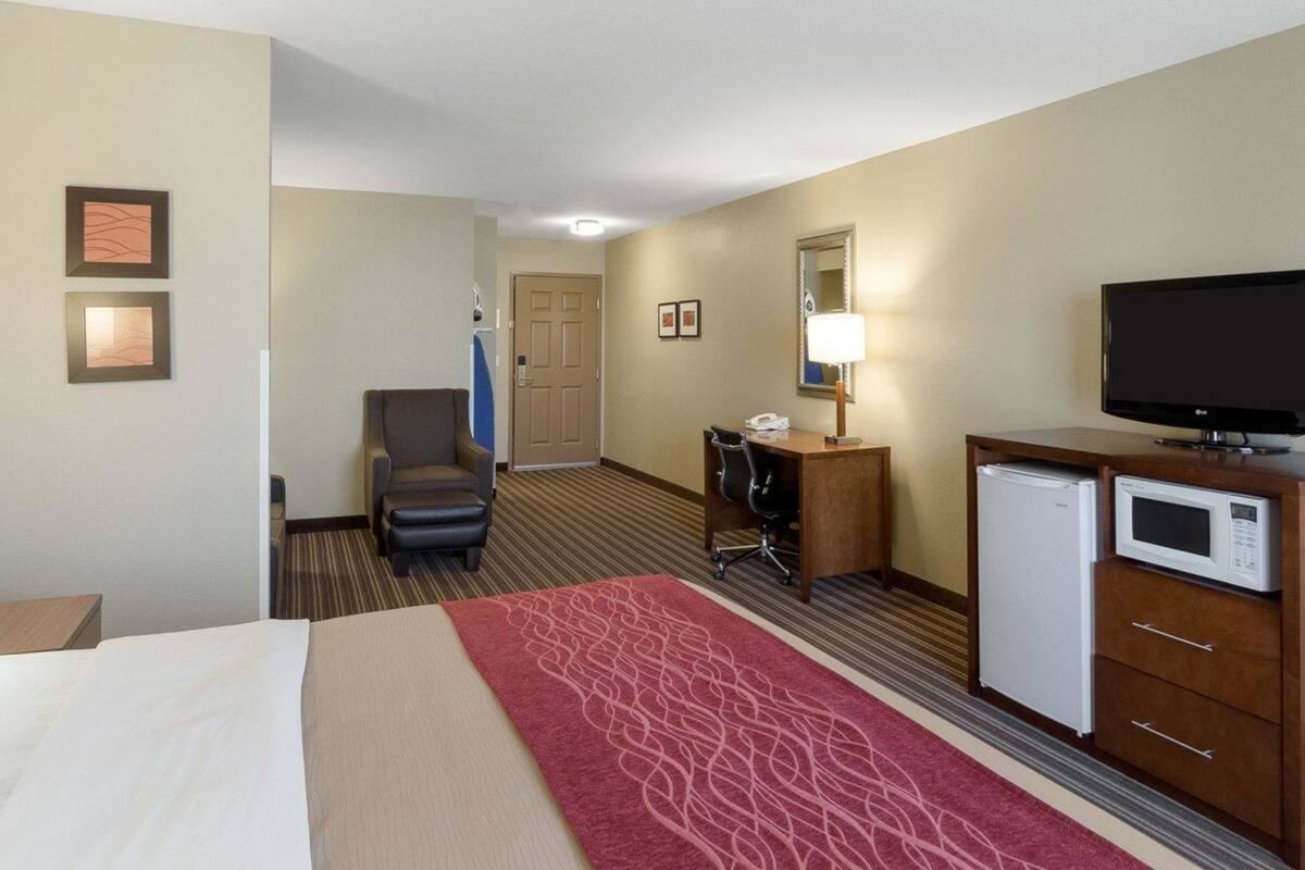 A hotel room with a bed, a desk with a computer, a television, a refrigerator, and a chair.