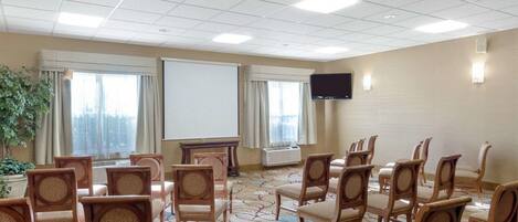 A conference room with rows of wooden chairs, a projector screen, a flat-screen TV, and a large window with curtains.