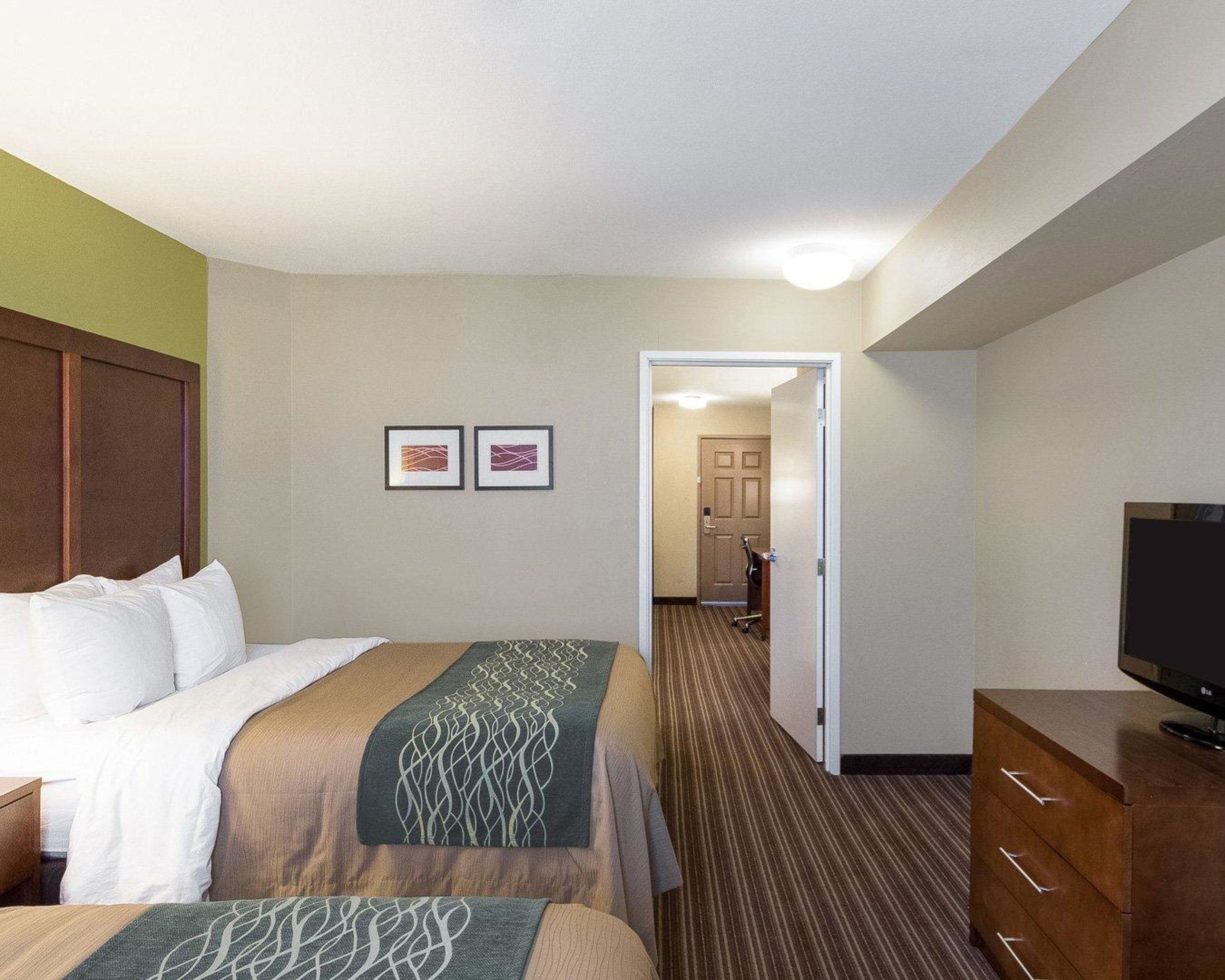 A hotel room with a bed, a desk, a television, and a hallway leading to a bathroom.