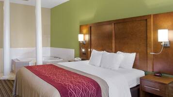 A hotel room with a large bed, a bedside table, a nightstand, a wall-mounted lamp, and a bathroom with a bathtub and sink.