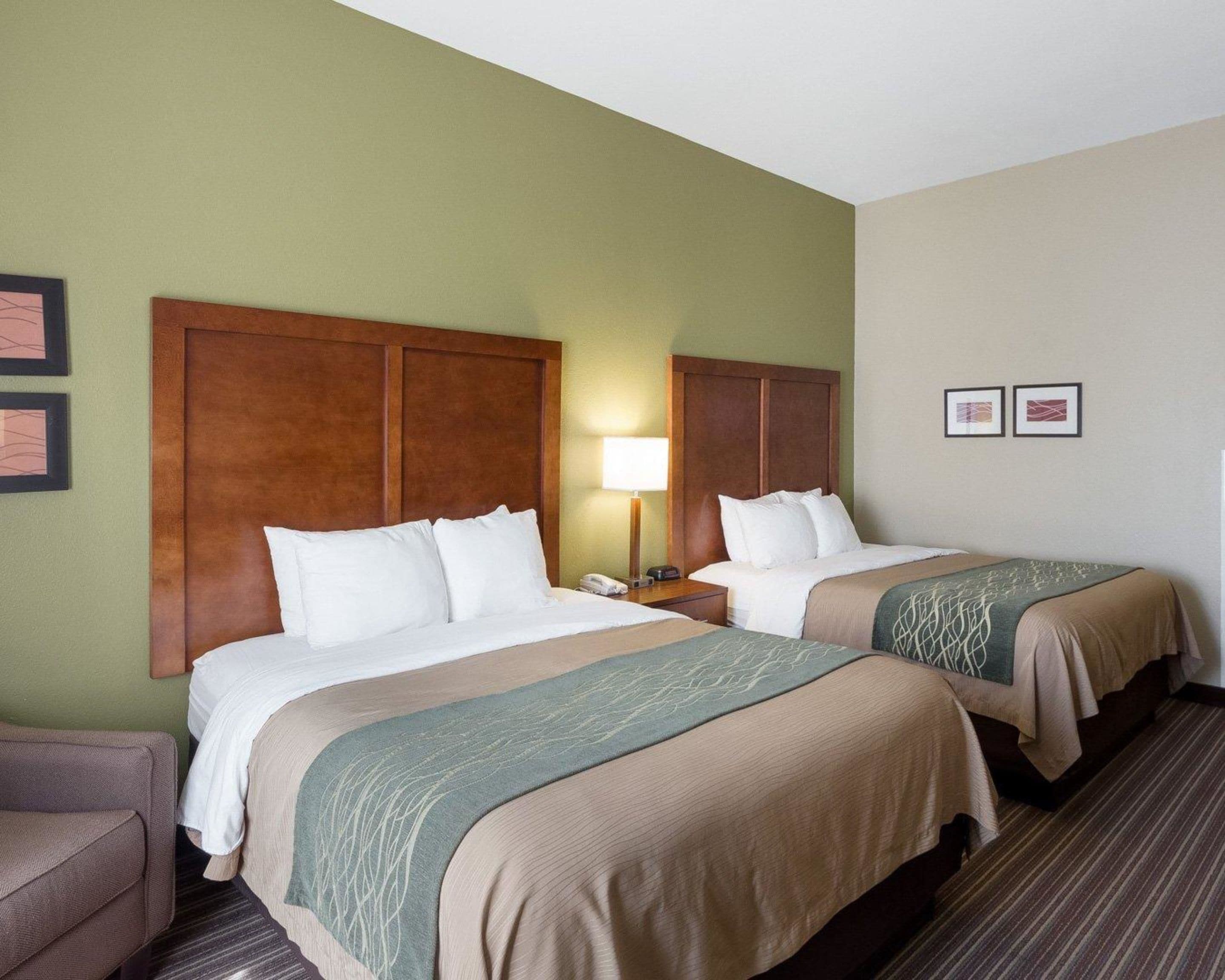 Habitación de hotel con dos camas, una mesita de noche, una lámpara y una silla.