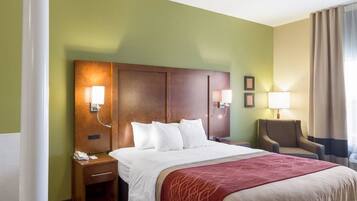 A hotel room with a large bed, a wooden headboard, bedside lamps, a chair, and a desk with a phone.