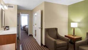 A hotel room with a bed, a desk, a chair, a lamp, and a bathroom with a mirror and sink. - Comfort Inn & Suites Fayetteville - University Area (Fayetteville)