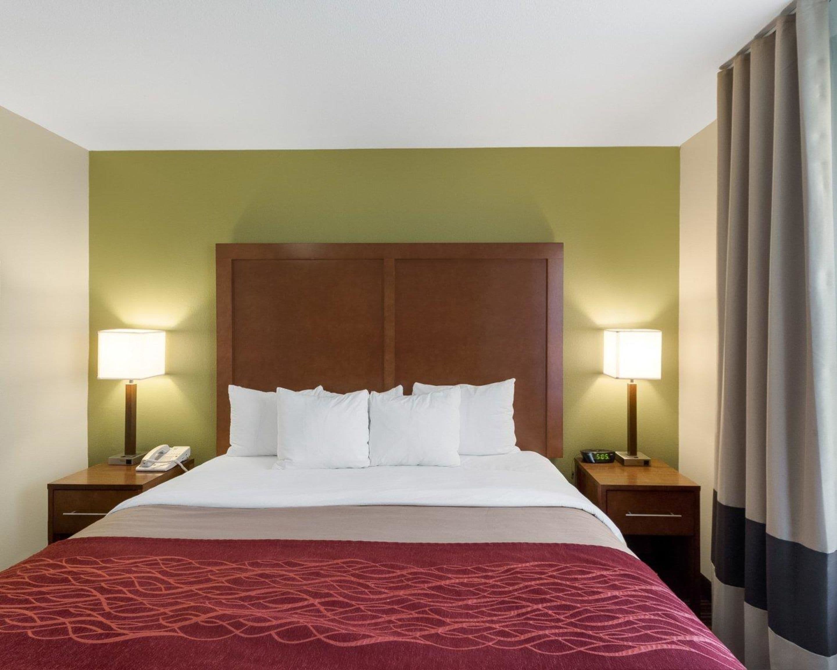 Una habitación de hotel con una cama grande, dos mesitas de noche con lámparas, un teléfono y un reloj.