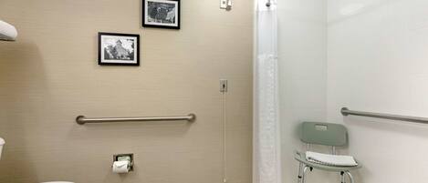 A bathroom with a toilet, two framed pictures on the wall, a handrail, a shower curtain, and a wheelchair.