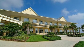 A large, multi-story hotel with a symmetrical facade, multiple balconies, and a well-maintained garden with palm trees.