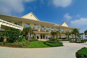 Un hotel grande de varios pisos con una fachada simétrica, múltiples balcones y un jardín cuidado con palmeras.