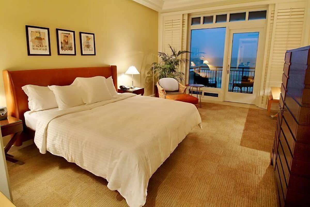 Ein Hotelzimmer mit einem großen Bett, einem Nachttisch, einem Sessel, einer Topfpflanze und einem Balkon mit Blick.