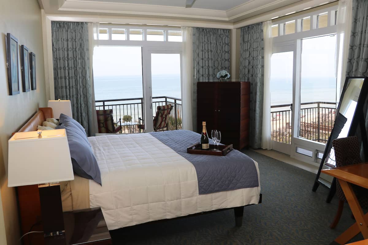 Ein Hotelzimmer mit einem großen Bett, einem Schreibtisch, einem Stuhl, einem Schminktisch und einem Balkon mit Meerblick.