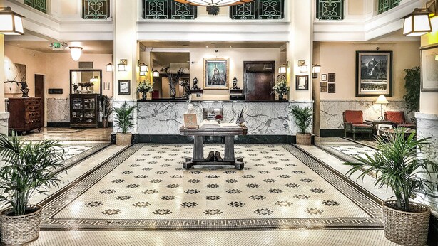 A spacious lobby with a marble floor, a reception desk, and a chandelier.
