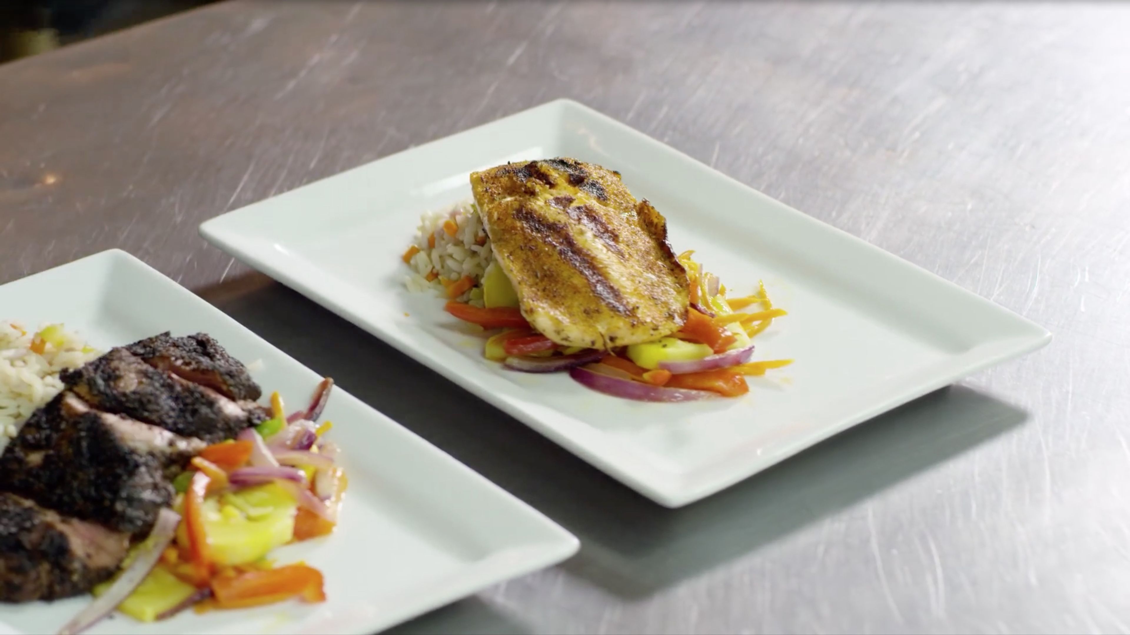 Two square white plates with food on a wooden table.