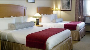 A hotel room with two beds, each with a red blanket, white linens, and decorative pillows. There are bedside lamps and a framed picture on the wall.