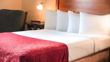 A neatly made bed with a wooden headboard, a red blanket, and white pillows.