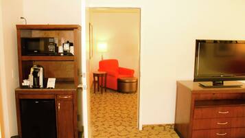 Habitación de hotel con kitchenette, televisor, un sillón rojo y una pequeña mesa.