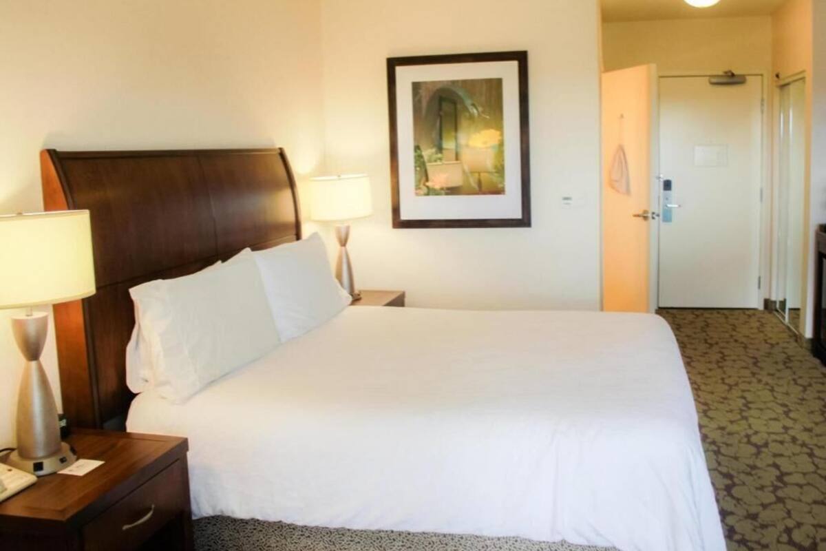 A hotel room with a bed, nightstands, a framed picture on the wall, and a door leading to another room.