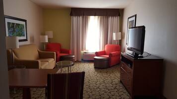 Une chambre d’hôtel avec un canapé, deux fauteuils, une télévision, une lampe et une moquette à motifs.