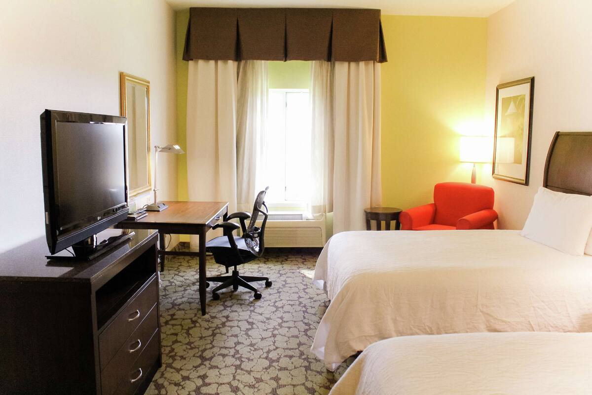 A hotel room with a bed, a desk with a computer, a chair, a television, and a lamp.