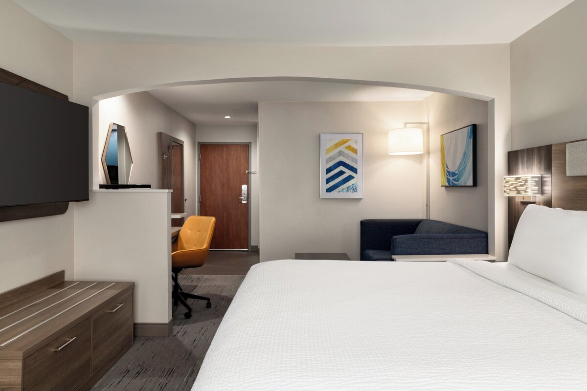 A hotel room with a large bed, a desk, a chair, and a TV mounted on the wall.