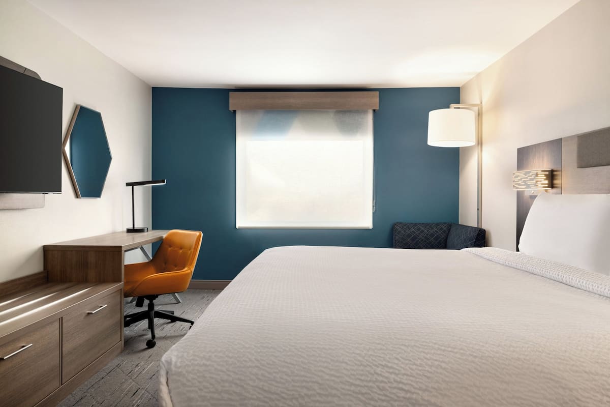 A hotel room with a bed, desk, chair, and a large window with a view.