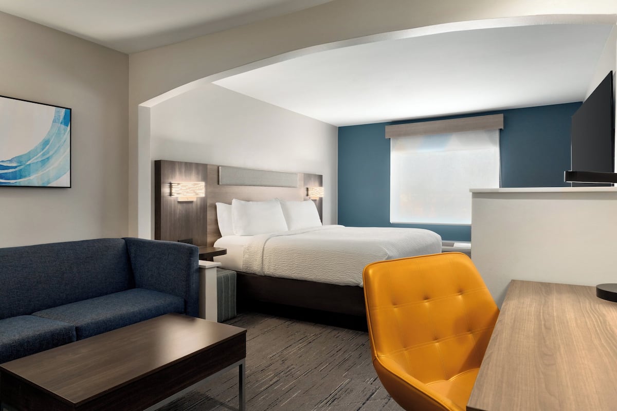 A hotel room with a bed, a sofa, a chair, a desk, and a TV.