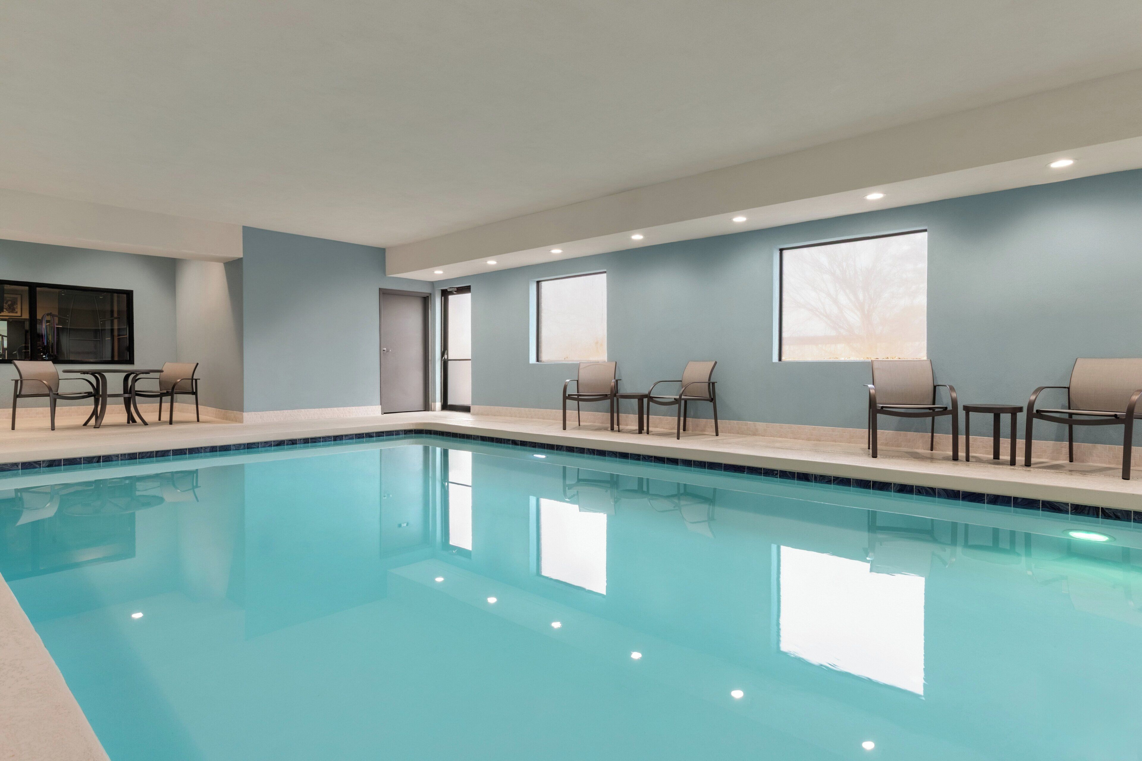 A swimming pool with chairs and tables, a door, and windows.