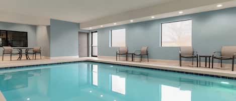 Una piscina con sillas y mesas, una puerta y ventanas.