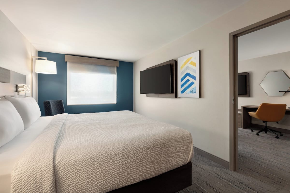 A hotel room with a bed, a desk, a chair, a TV, and artwork on the wall.
