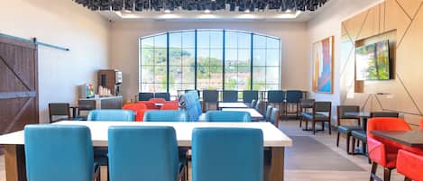 A modern dining area with a large window, wooden ceiling, and blue chairs.