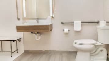 Un baño moderno con tocador de madera, inodoro con barra de apoyo y espejo sobre el lavamanos.