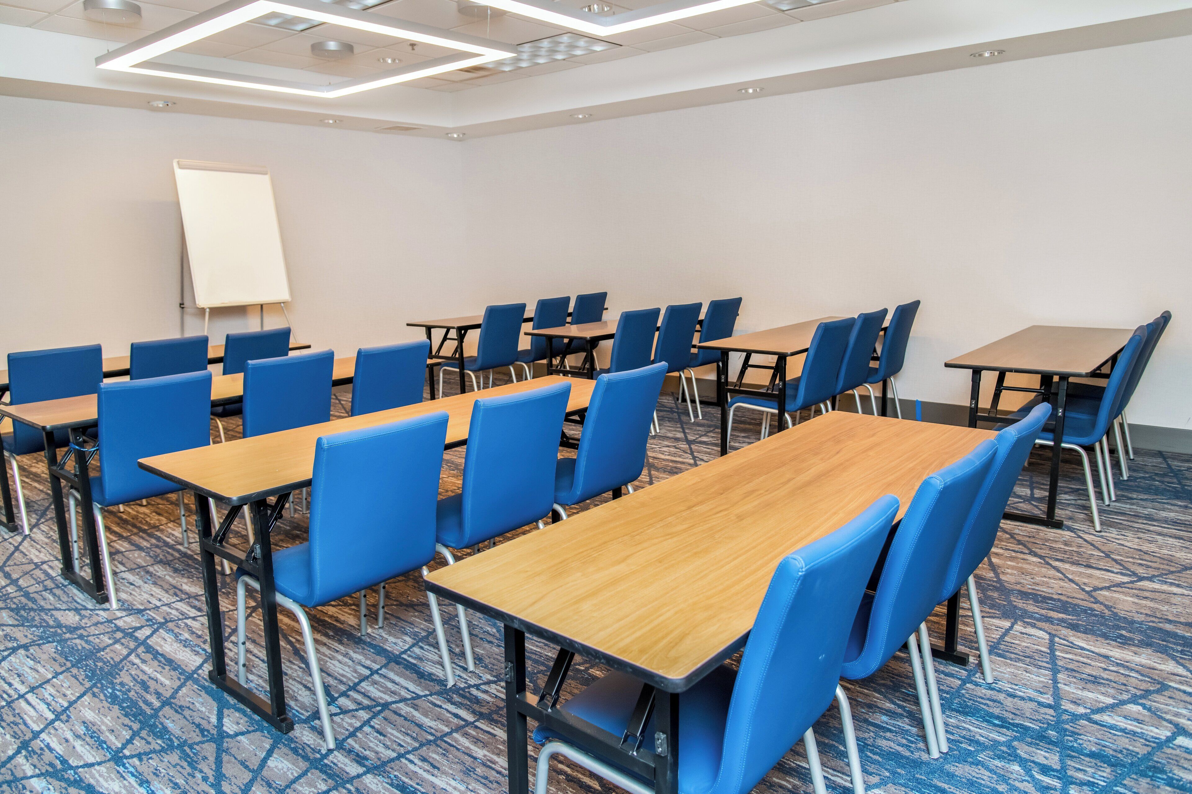 Un salón de conferencias con sillas azules y mesas de madera, una pizarra y alfombra estampada.