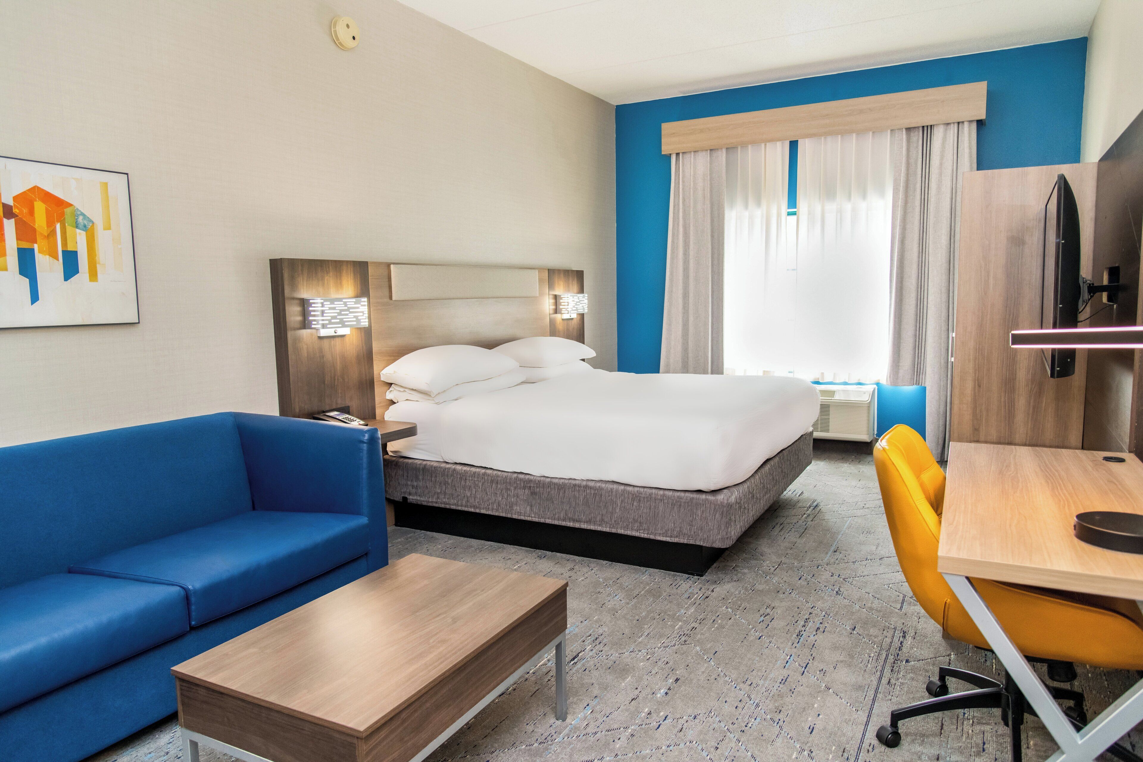 A hotel room with a bed, a blue sofa, a wooden desk, and a chair.