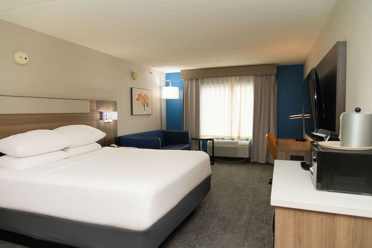 A hotel room with a large bed, a desk with a computer, a television, and a window with curtains.