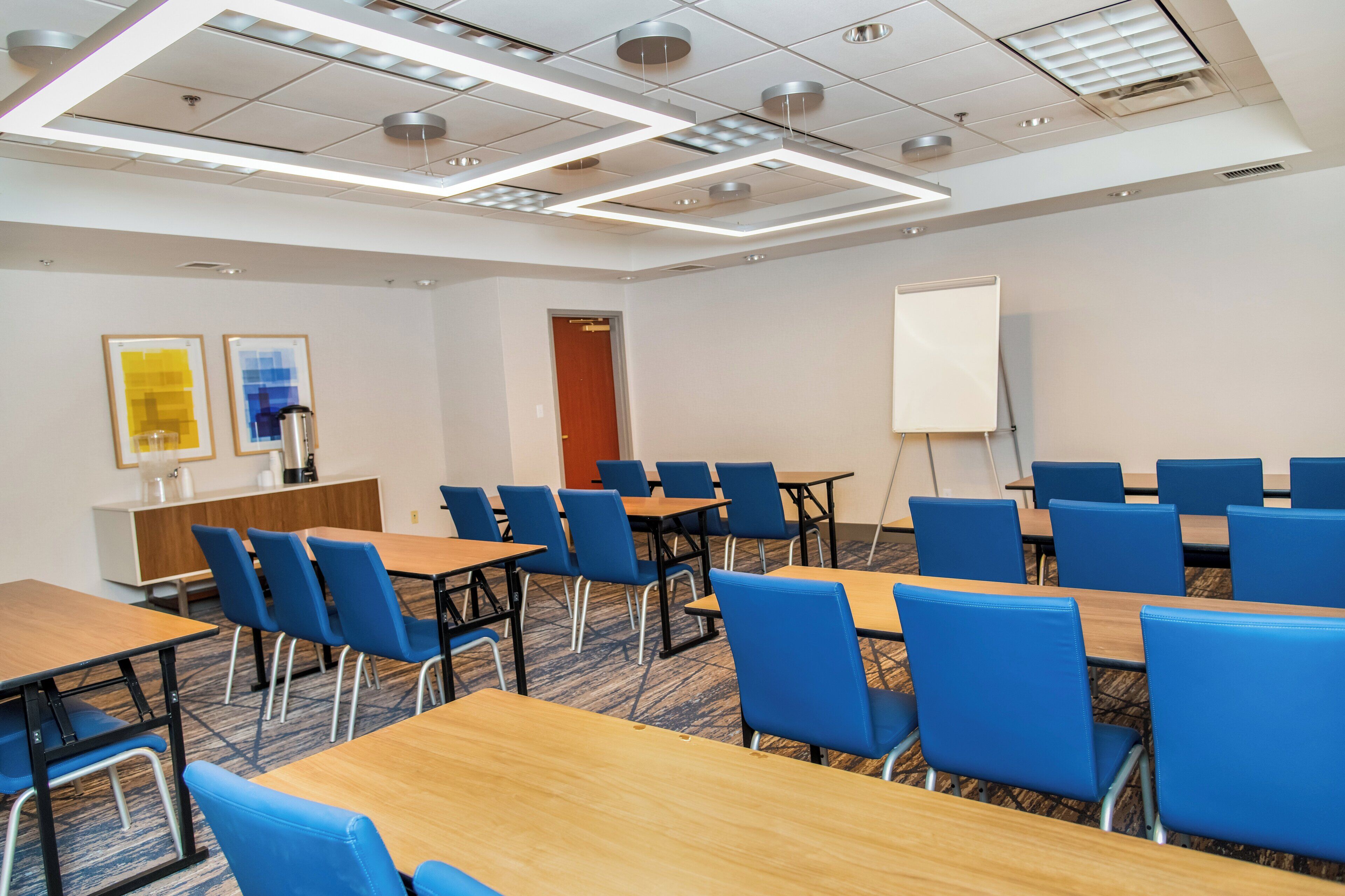 Un salón de conferencias con mesas y sillas, una pizarra y una puerta al fondo.