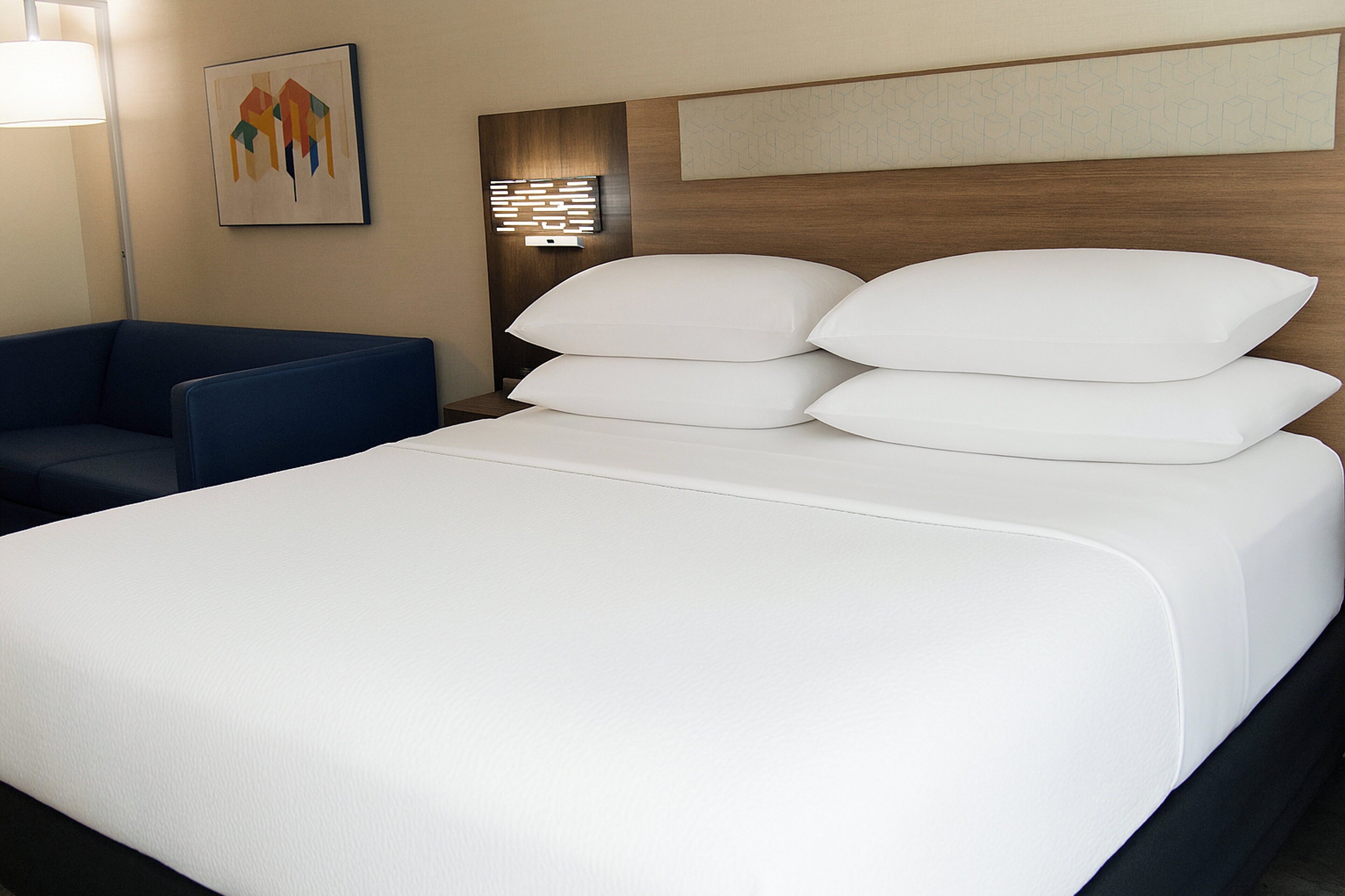 Habitación de hotel con una cama grande, un sillón azul y una obra de arte en la pared.