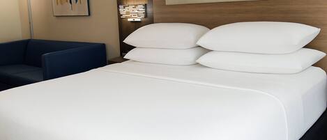 Habitación de hotel con una cama grande, un sillón azul y una obra de arte en la pared.