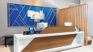 A hotel reception desk with a modern design, a large blue geometric wall art piece, and a wooden partition. - Holiday Inn Express Hotel & Suites Pittsburgh-South Side by IHG (Pittsburgh)