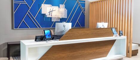 A hotel reception desk with a modern design, a large blue geometric wall art piece, and a wooden partition.