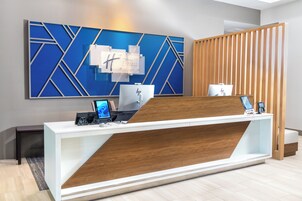Balcão de recepção de hotel com design moderno, uma grande obra de arte geométrica azul na parede e um painel de madeira.