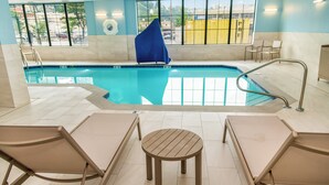 An indoor swimming pool with clear glass walls, a blue chair, and a small round table in the center. - Holiday Inn Express Hotel & Suites Pittsburgh-South Side by IHG (Pittsburgh)