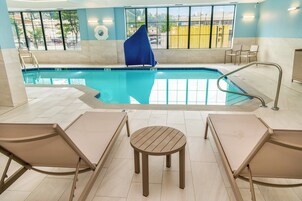 Uma piscina interior com paredes de vidro transparente, uma cadeira azul e uma pequena mesa redonda no centro.