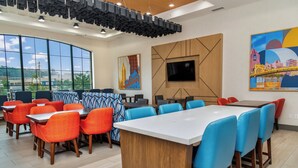 A modern dining area with high tables and chairs, large windows, and artwork on the walls. - Holiday Inn Express Hotel & Suites Pittsburgh-South Side by IHG (Pittsburgh)