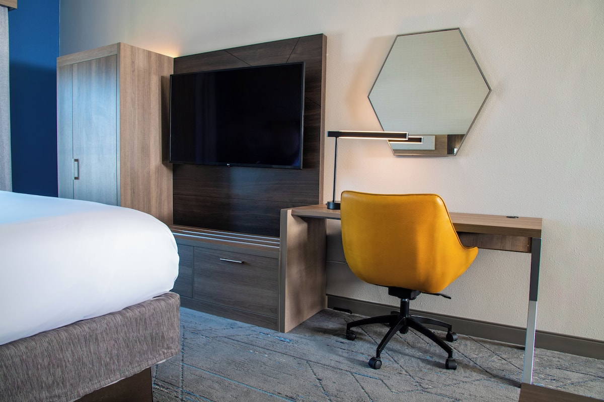 A hotel room with a bed, a desk, a chair, a TV, and a mirror.